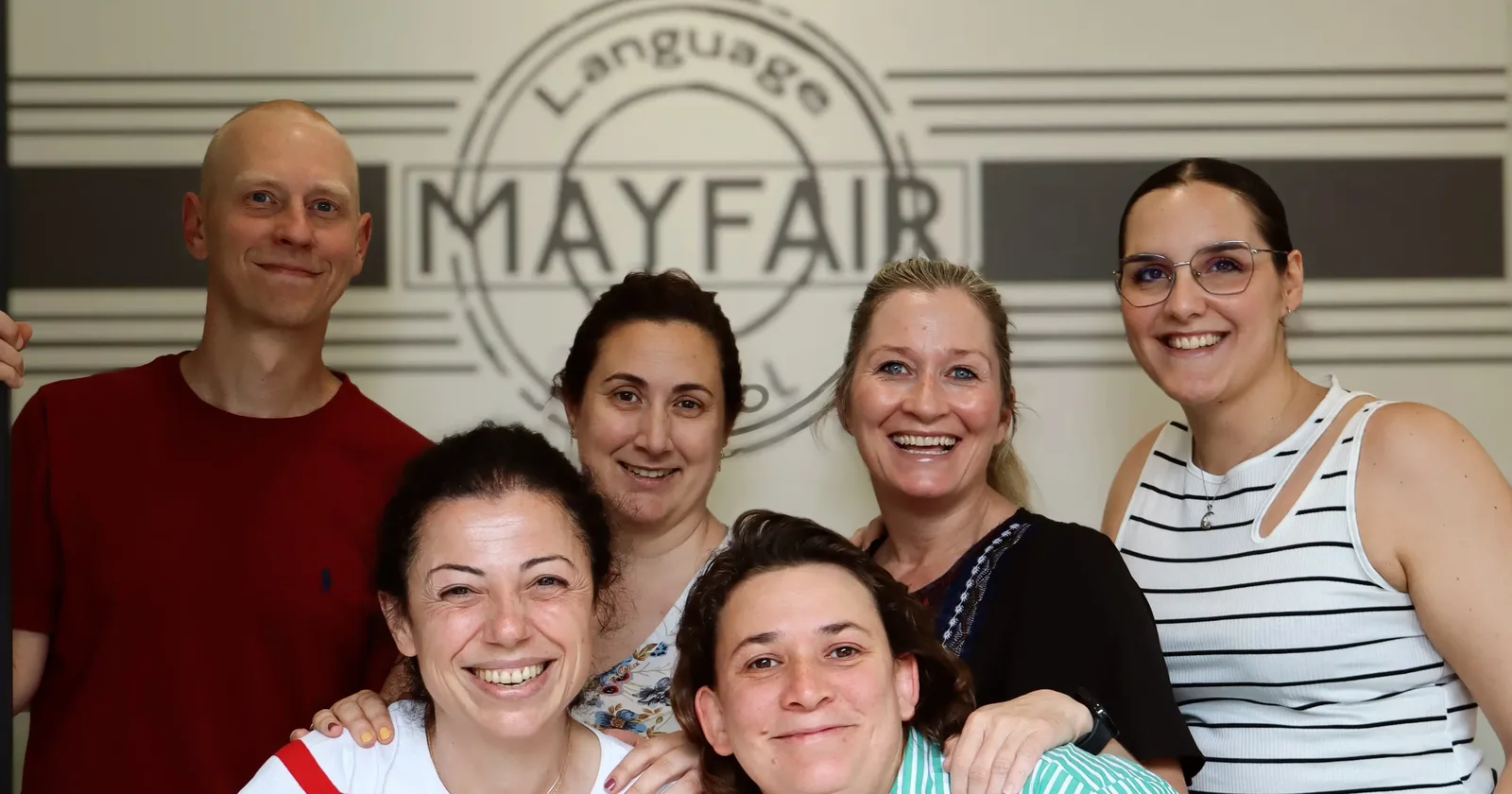 El equipo de profesores de MayFair School Córdoba, sonriente frente al logo de la academia